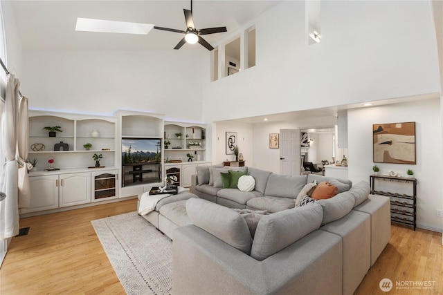 living area with ceiling fan, light wood-style flooring, a high ceiling, and a skylight