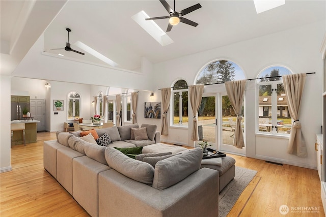 living room with light wood finished floors, visible vents, ceiling fan, a skylight, and high vaulted ceiling