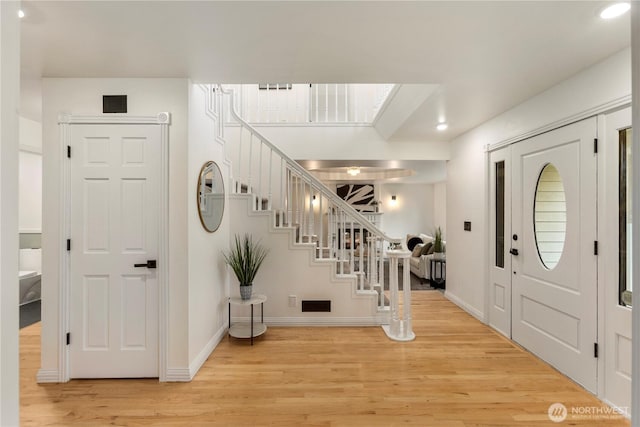 entryway with light wood finished floors, stairway, visible vents, and baseboards