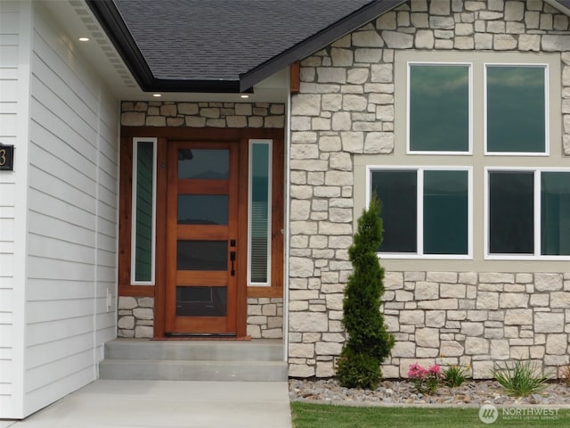 entrance to property with stone siding and roof with shingles