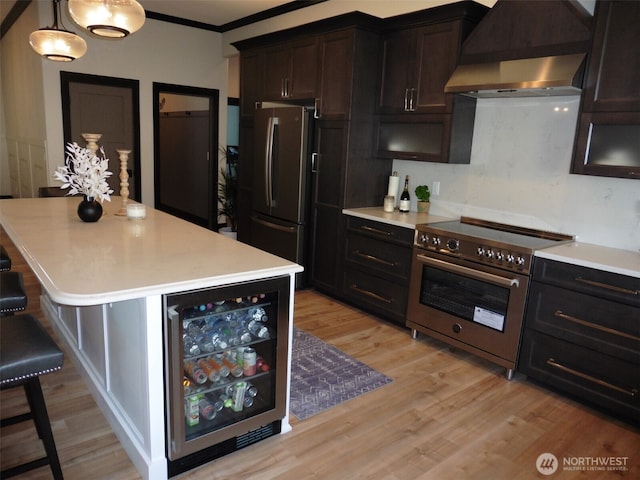 kitchen featuring beverage cooler, freestanding refrigerator, stainless steel stove, wall chimney range hood, and light wood-type flooring