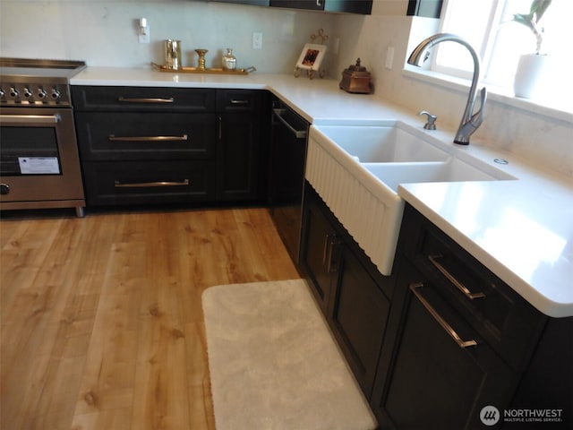 kitchen with light wood-type flooring, light countertops, dark cabinetry, stainless steel range, and a sink