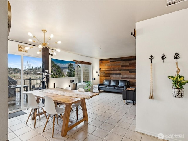 dining space featuring an inviting chandelier, light tile patterned floors, visible vents, and wood walls