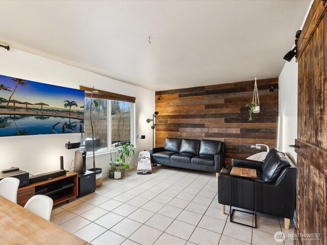 living area featuring light tile patterned floors, wood walls, an accent wall, and a barn door