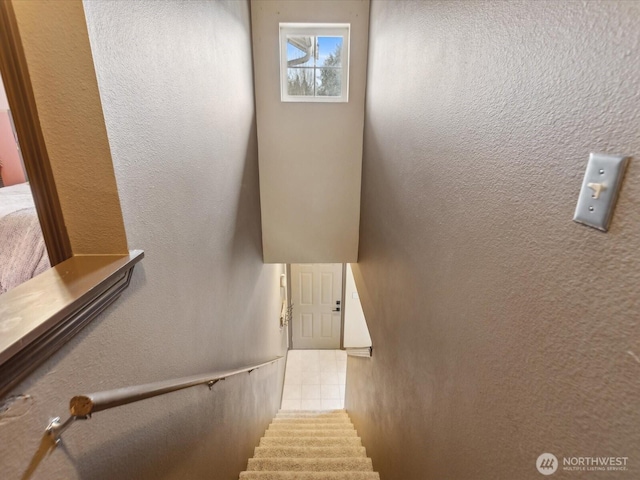 stairs with tile patterned floors and a textured wall