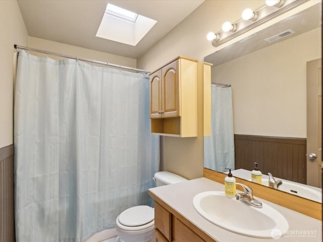 full bathroom featuring vanity, a wainscoted wall, visible vents, a skylight, and toilet