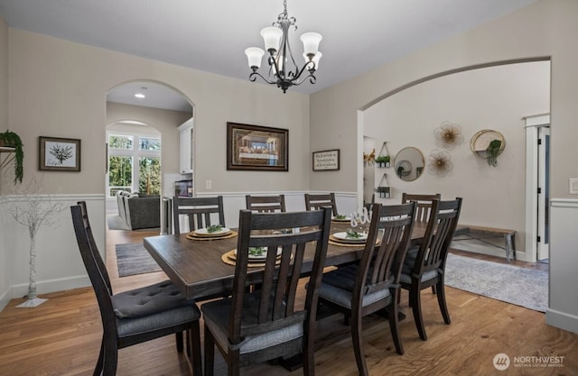 dining room with arched walkways, a chandelier, light wood finished floors, and baseboards