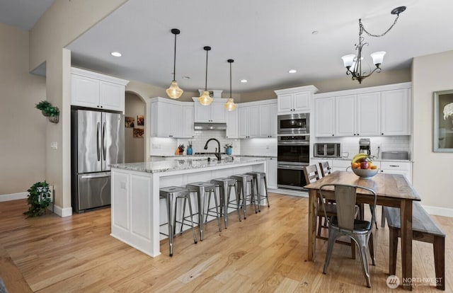 kitchen with under cabinet range hood, white cabinets, appliances with stainless steel finishes, and a sink