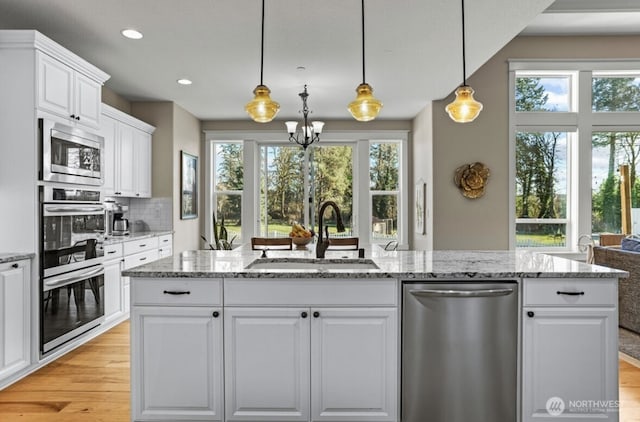 kitchen featuring light stone countertops, a sink, white cabinets, light wood-style floors, and appliances with stainless steel finishes