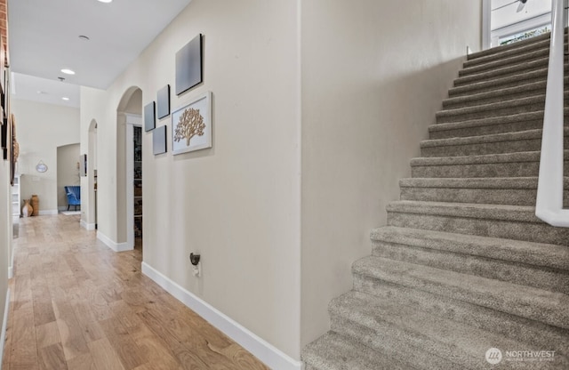 stairway with recessed lighting, wood finished floors, arched walkways, and baseboards