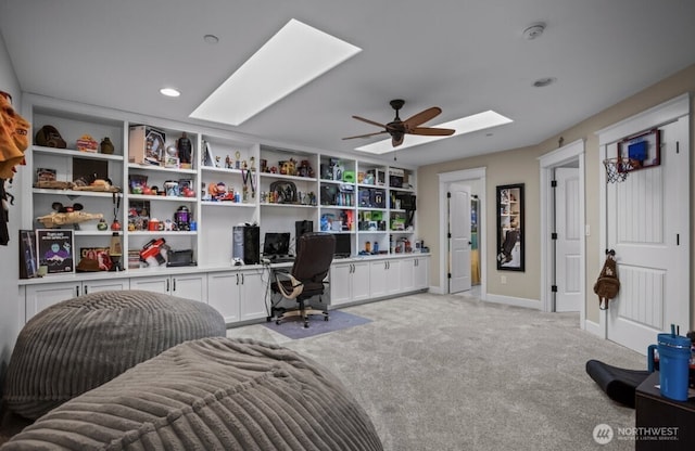 home office featuring a ceiling fan, a skylight, baseboards, light colored carpet, and built in study area