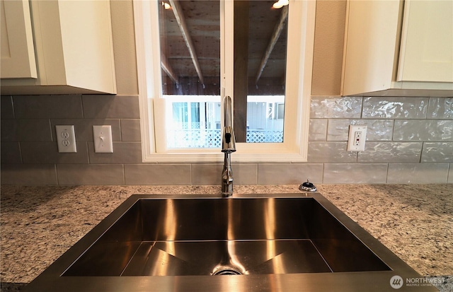 room details featuring a sink, decorative backsplash, light stone countertops, and white cabinetry