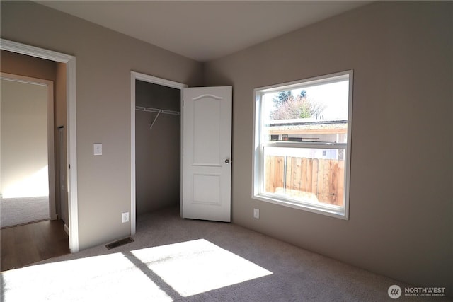 unfurnished bedroom featuring a closet, visible vents, multiple windows, and carpet flooring