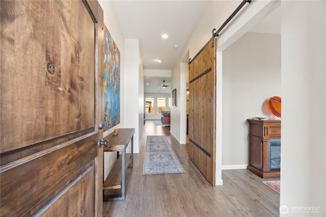 hall with baseboards, a barn door, and wood finished floors