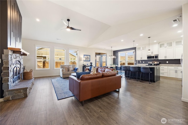 living area with visible vents, ceiling fan, vaulted ceiling, a fireplace, and dark wood-style flooring