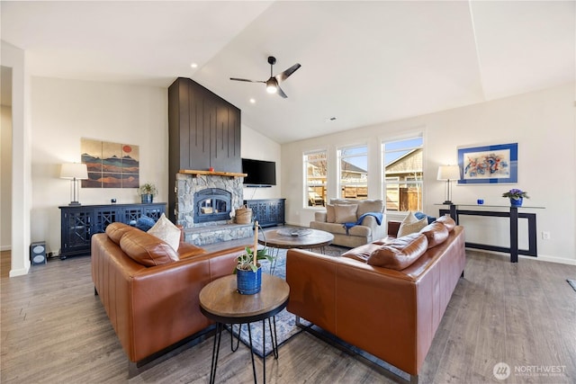 living area with a ceiling fan, wood finished floors, a fireplace, baseboards, and vaulted ceiling