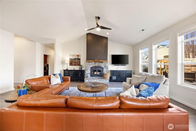 living room with visible vents, vaulted ceiling, a stone fireplace, wood finished floors, and a ceiling fan