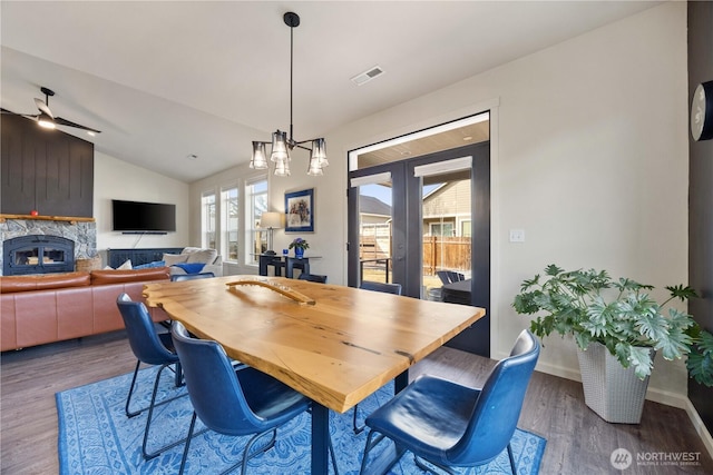 dining area with french doors, lofted ceiling, wood finished floors, and a fireplace