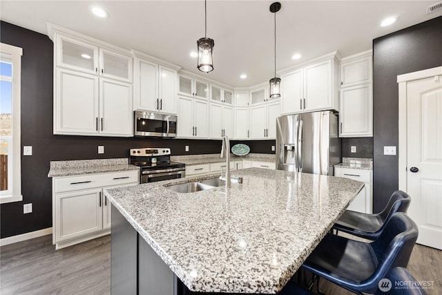 kitchen featuring a sink, wood finished floors, white cabinetry, stainless steel appliances, and a breakfast bar area