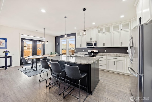 kitchen with light wood-type flooring, a sink, stainless steel appliances, french doors, and light stone countertops