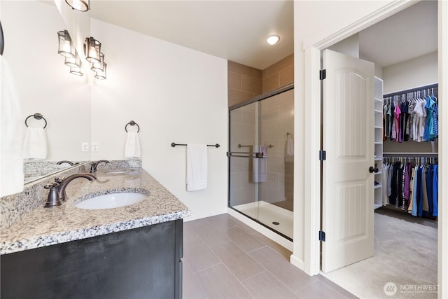 bathroom with a walk in closet, a shower stall, double vanity, and a sink