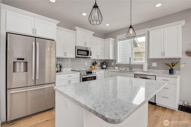 kitchen with a sink, light stone counters, stainless steel appliances, white cabinets, and light wood finished floors