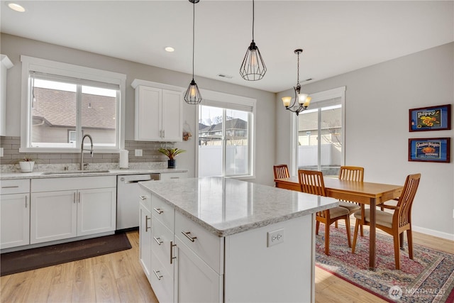 kitchen with a sink, backsplash, light wood-type flooring, and stainless steel dishwasher