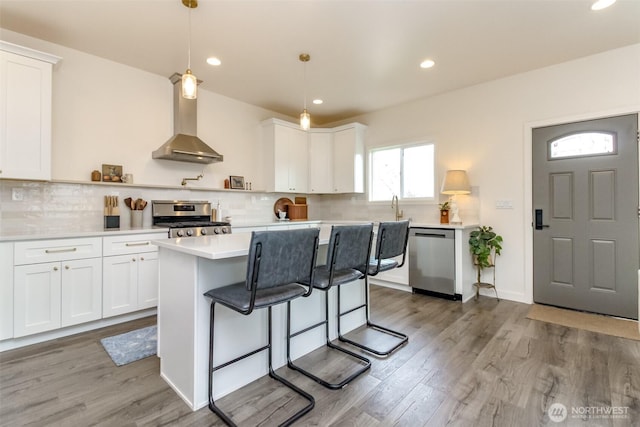 kitchen featuring wood finished floors, white cabinetry, stainless steel appliances, wall chimney exhaust hood, and light countertops