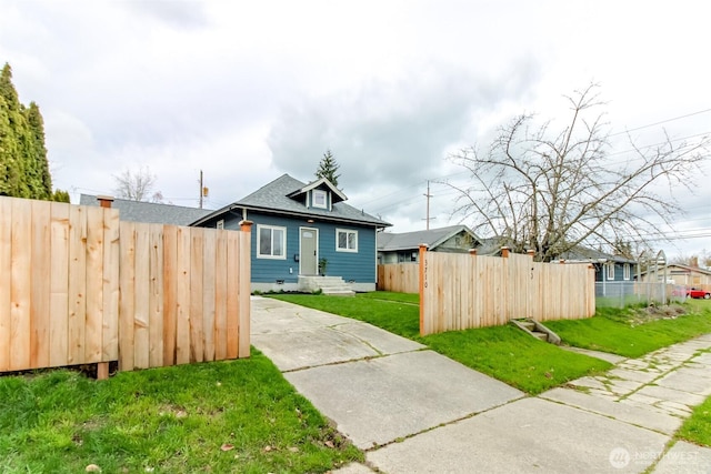 bungalow featuring roof with shingles, a front yard, and fence