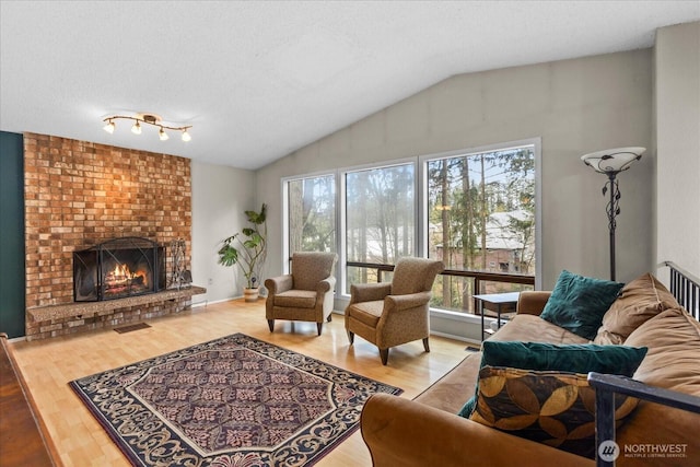 living area featuring vaulted ceiling, wood finished floors, a fireplace, and a textured ceiling