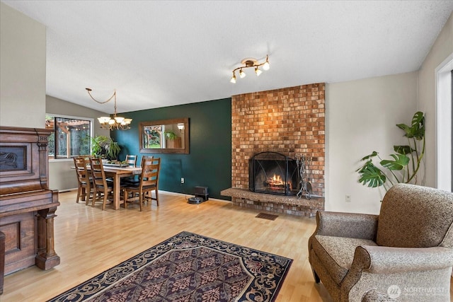 living room with a textured ceiling, a brick fireplace, wood finished floors, and vaulted ceiling