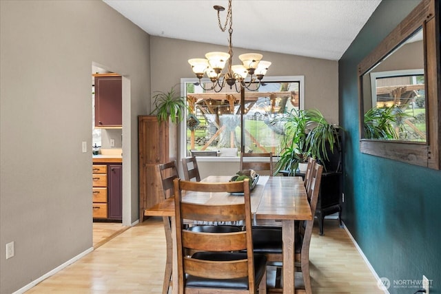 dining room with light wood finished floors, a notable chandelier, baseboards, and vaulted ceiling