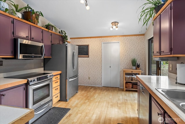 kitchen featuring wallpapered walls, light wood-type flooring, light countertops, stainless steel appliances, and a sink