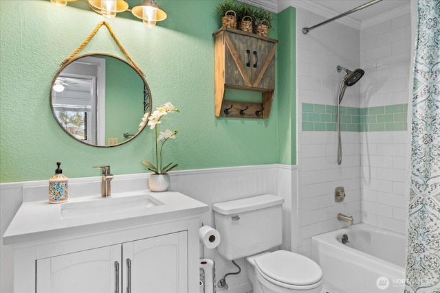 full bath featuring shower / bathtub combination with curtain, toilet, wainscoting, crown molding, and vanity