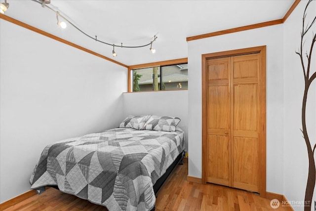 bedroom with rail lighting, light wood-style floors, baseboards, and ornamental molding