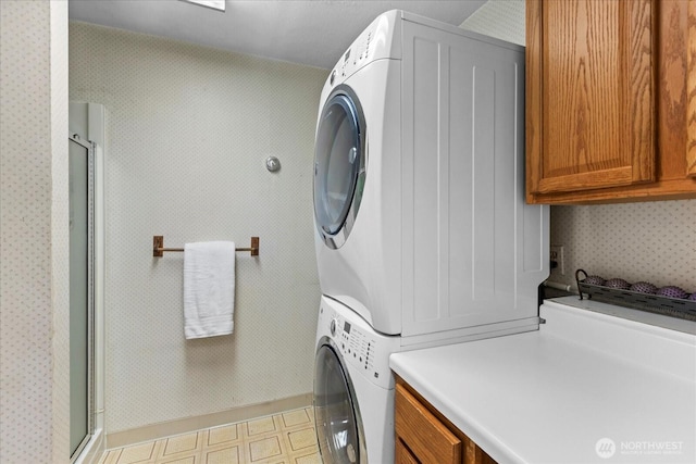 clothes washing area with stacked washer / drying machine, cabinet space, and light floors