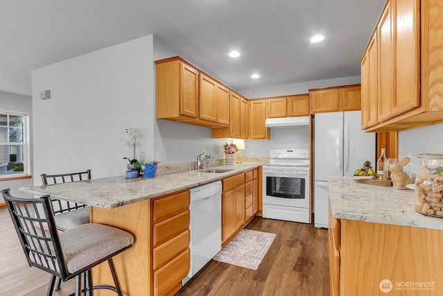 kitchen featuring under cabinet range hood, a kitchen breakfast bar, dark wood-style floors, white appliances, and a sink