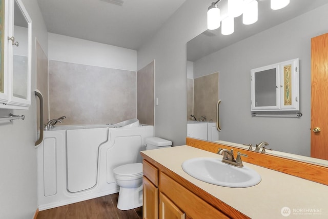 bathroom featuring a bath, toilet, vanity, and wood finished floors