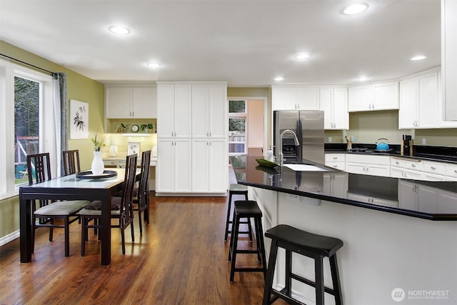 kitchen featuring a kitchen bar, stainless steel refrigerator with ice dispenser, dark countertops, dark wood finished floors, and white cabinetry