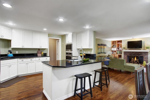 kitchen featuring a sink, dark wood-style floors, white cabinetry, stainless steel appliances, and a fireplace