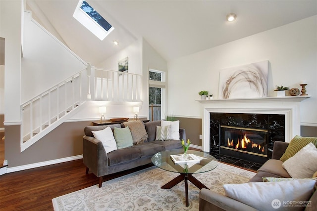 living room with high vaulted ceiling, wood finished floors, stairway, a skylight, and a premium fireplace