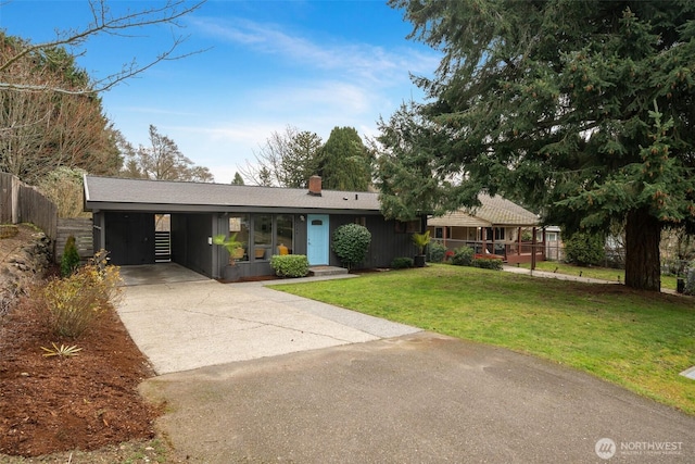 view of front of property with fence, concrete driveway, a front yard, an attached carport, and a chimney