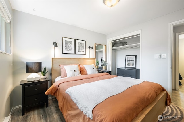 bedroom featuring a closet, a baseboard heating unit, and wood finished floors