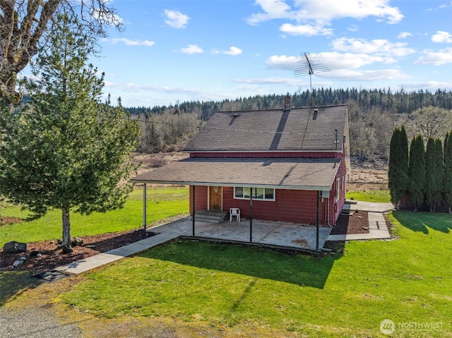 rear view of property featuring a yard, entry steps, a forest view, and a patio