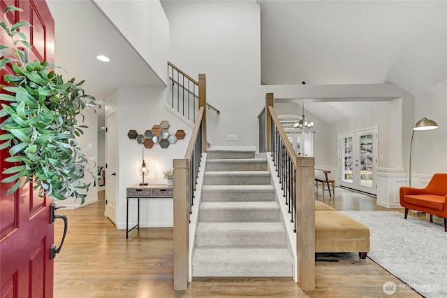 entrance foyer featuring high vaulted ceiling, wood finished floors, stairway, french doors, and an inviting chandelier