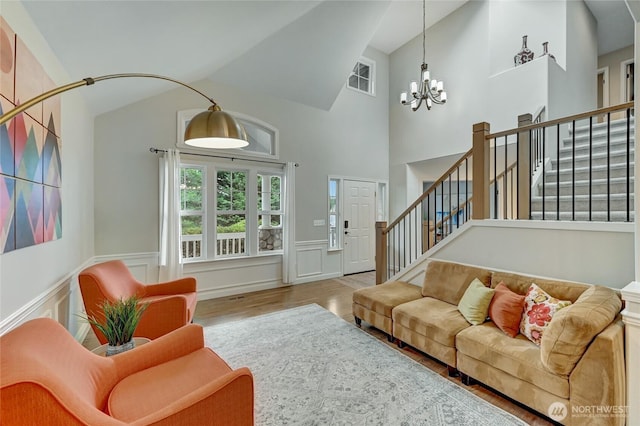 living area featuring visible vents, wood finished floors, an inviting chandelier, wainscoting, and stairs