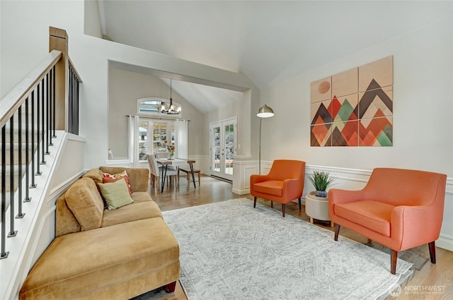 living room with wood finished floors, stairs, vaulted ceiling, wainscoting, and a chandelier