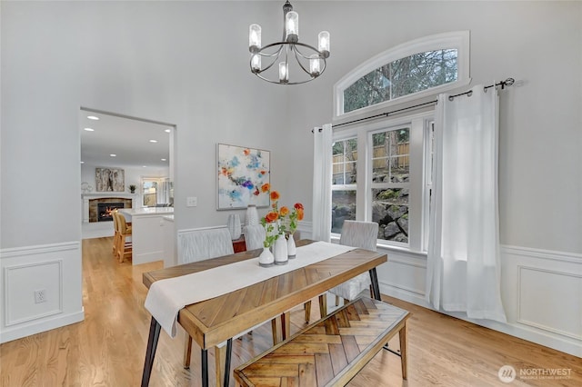 dining space featuring a wainscoted wall, a warm lit fireplace, and light wood finished floors