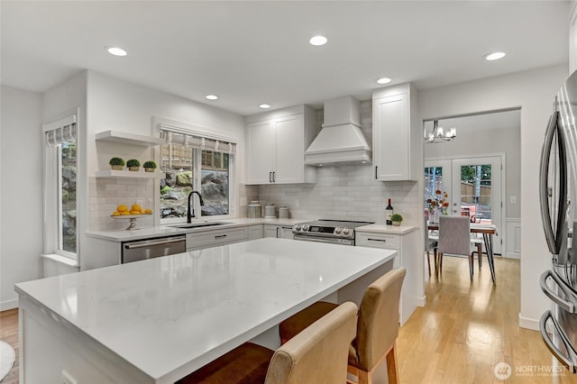 kitchen with custom range hood, light wood finished floors, appliances with stainless steel finishes, and a sink