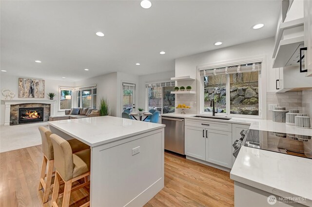 kitchen featuring a kitchen island, dishwasher, exhaust hood, a glass covered fireplace, and a sink